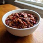 A close-up of a white bowl filled with rich, thick Slow Cooker Lentil Taco Chili featuring kidney beans.