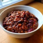 A white bowl filled with rich, dark red Slow Cooker Lentil Taco Chili featuring visible kidney beans.
