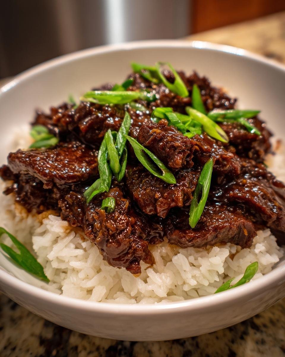Close-up of Slow Cooker Mongolian Beef, rich and glossy, served over white rice and garnished with fresh green onions.