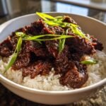 Close-up of tender Slow Cooker Mongolian Beef coated in rich sauce served over white rice and garnished with green onions.