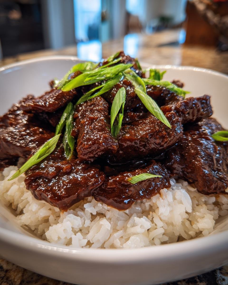 Close-up of tender Slow Cooker Mongolian Beef coated in rich sauce served over white rice and topped with green onions.