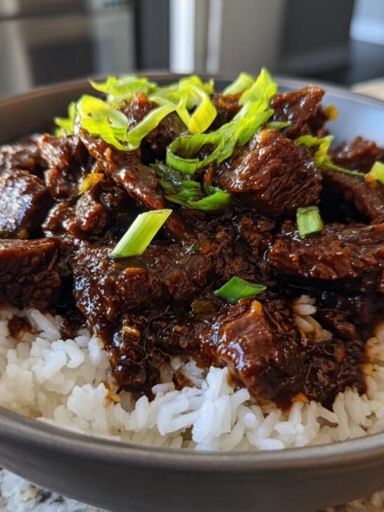 Close-up of tender Slow Cooker Mongolian Beef coated in rich sauce served over white rice and topped with green onions.