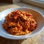 Close-up of a white bowl filled with saucy, shredded Slow Cooker Shredded Mexican Chicken.