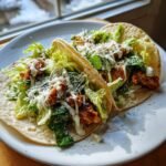 Two delicious Smash Chicken Caesar Tacos filled with seasoned chicken, romaine lettuce, and drizzled with Caesar dressing and Parmesan.