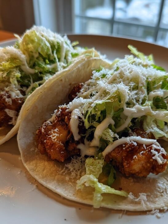 Two delicious Smash Chicken Caesar Tacos filled with crispy chicken, shredded lettuce, cheese, and Caesar dressing.