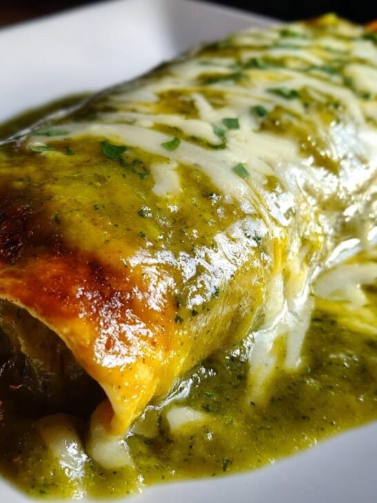 A close-up view of a perfectly Smothered Green Chile Chicken Burrito covered in rich green sauce and melted white cheese.