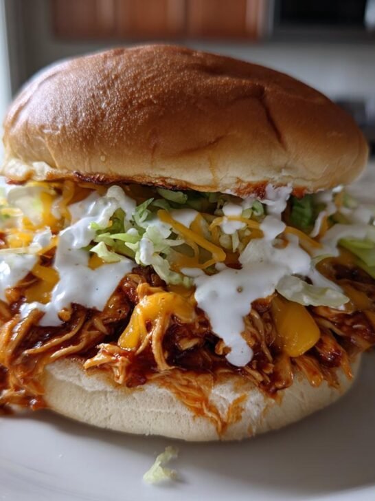 Close-up of a Spicy Shredded Buffalo Chicken Sandwich piled high with sauce, cheese, lettuce, and ranch drizzle.