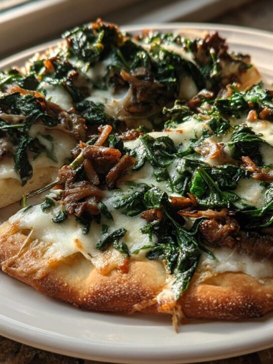 Two slices of Spinach Mushroom Naan Pizza topped with melted white cheese, saut&eacute;ed spinach, and mushrooms on a white plate.