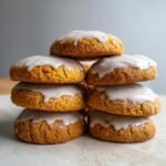 A tall stack of soft, orange Glazed Pumpkin Cookies topped with thick white vanilla icing.
