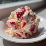 A scoop of creamy Strawberry Shortcake Fluff Salad mixed with visible chunks of fresh strawberries on a white plate.