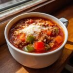 Close-up of a white bowl filled with rich Stuffed Pepper Soup, featuring ground meat, rice, peppers, and melted cheese on top.
