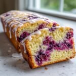 Close-up of a slice of Swirled Blackberry Lavender Sheet Cake showing the moist yellow crumb and deep purple berry swirl, drizzled with white icing.