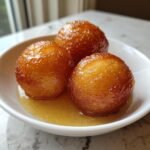 Close-up of three golden brown, syrup-soaked Gulab Jamun resting in a small white bowl.