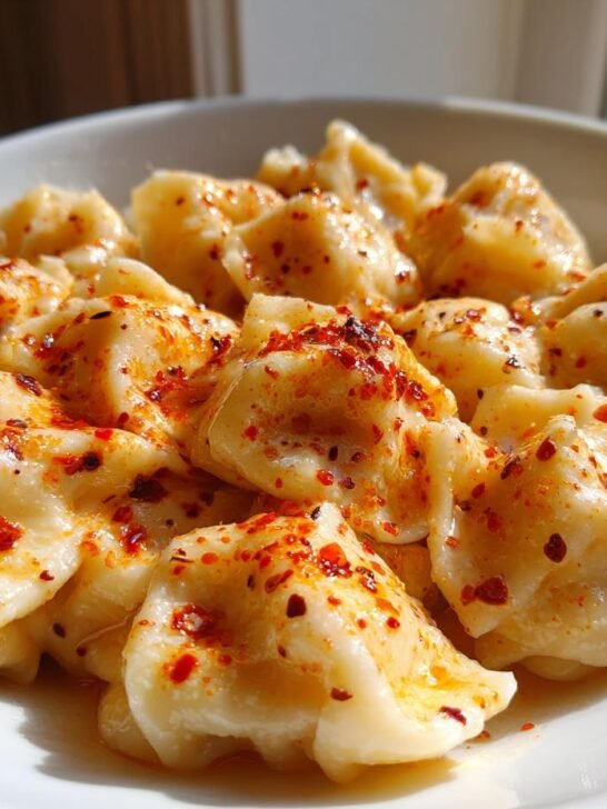 Close-up of Turkish Pasta (Manti/Dumplings) served in a white bowl, drizzled with melted butter and red chili flakes.