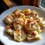 Close-up of Turkish Pasta Recipe (Manti) covered in creamy yogurt sauce and sprinkled with red pepper flakes.