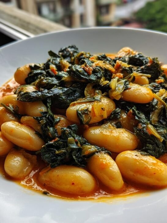 A close-up of creamy white butter beans coated in a rich, orange sauce and topped with wilted dark greens, representing Tuscan Marry Me Butter Beans.