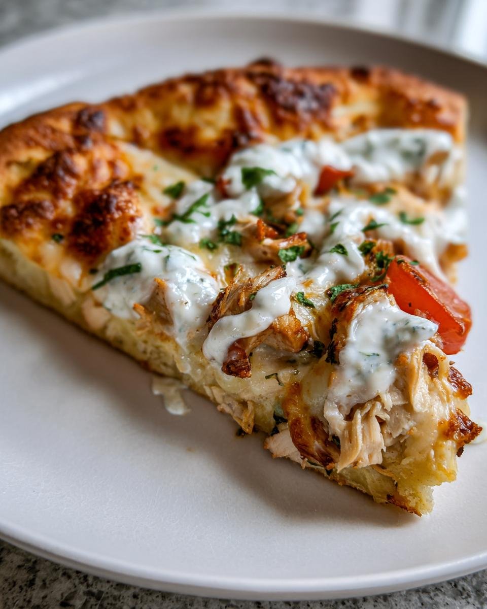 Close-up of a slice of Tzatziki Chicken Pizza showing shredded chicken, melted cheese, and a drizzle of white tzatziki sauce.