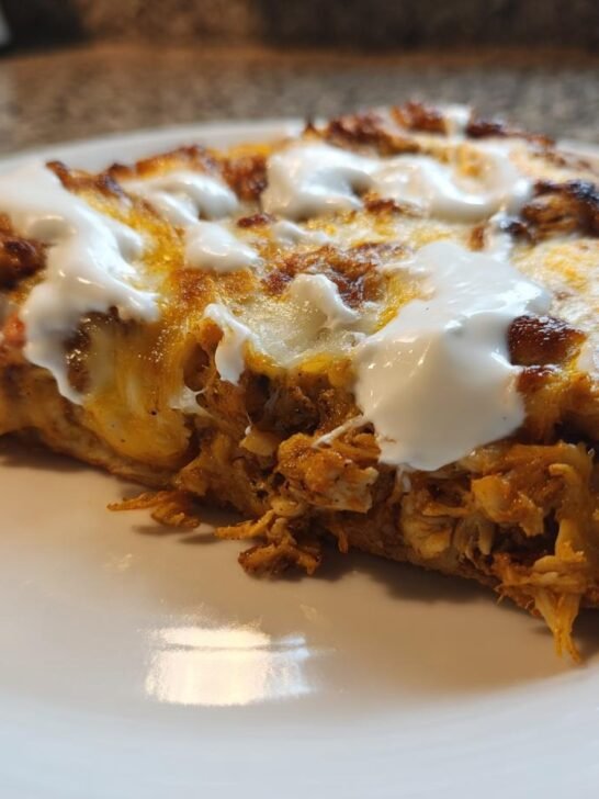 A close-up of a thick slice of Tzatziki Chicken Pizza showing shredded chicken, melted cheese, and dollops of white sauce.