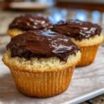 Three moist vanilla cupcakes topped generously with thick, glossy chocolate frosting.