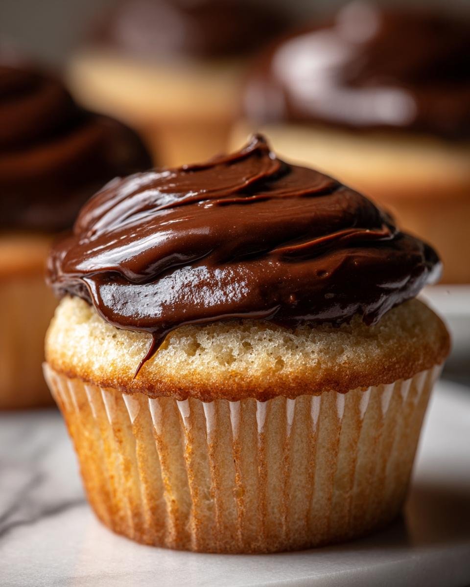 A close-up, macro shot of one perfect Vanilla Cupcakes With Chocolate Frosting, showing rich, glossy frosting.