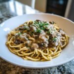 A close-up of creamy Vegan Mushroom Stroganoff served over pasta noodles and garnished with fresh parsley.