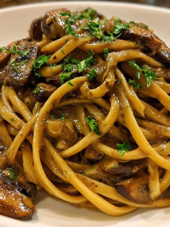 Close-up of creamy Vegan Mushroom Stroganoff served over thick pasta noodles, garnished with parsley.