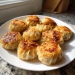 A plate of golden brown Viral One Pan Baked Dumplings with crispy, seared tops, served indoors.