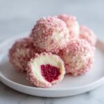 Close-up of White Chocolate Raspberry Truffles coated in pink crumbs, one cut open revealing a vibrant raspberry filling.