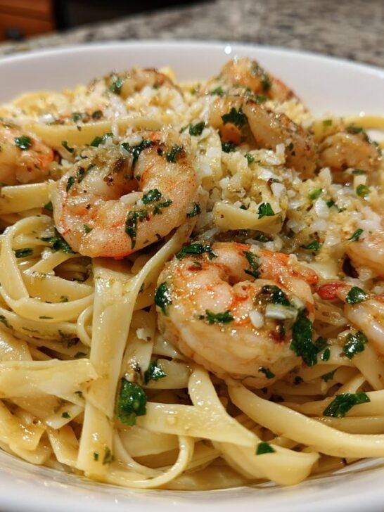 Close-up of a white bowl filled with Zesty One Pan Lemon Garlic Shrimp Pasta, topped with shrimp and fresh parsley.