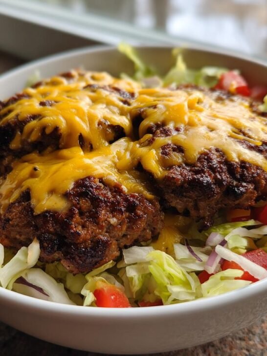 A white bowl filled with fresh lettuce, diced tomatoes, and topped with cheesy, seasoned burger patties for amazing Burger Bowls.