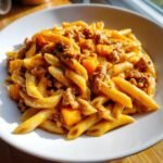 A bowl of creamy Autumn Sausage Pasta Squash featuring penne pasta, ground sausage, and orange squash cubes.