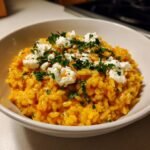 A close-up of creamy, orange Baked Pumpkin Goat Cheese Risotto topped with dollops of white goat cheese and fresh parsley.