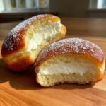 Two halves of a Brioche Doughnut With Cheesecake filling, showing the fluffy interior and creamy filling, dusted with powdered sugar.