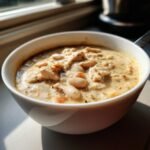 Close-up of a white bowl filled with creamy Cajun White Chicken Chili, showing chunks of chicken and white beans.