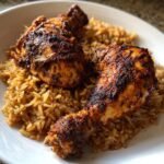Two pieces of richly seasoned Caribbean Jerk Chicken And Rice served on a white plate.