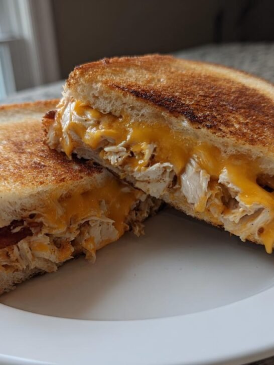 Two halves of a grilled Cheddar Bacon Ranch Chicken Melt showing melted cheese, shredded chicken, and crispy bacon.