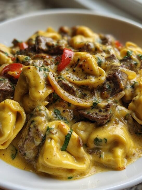 A close-up of cheesy tortellini pasta mixed with steak pieces and peppers in a rich Cheesesteak Tortellini Provolone Sauce.