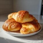 A stack of golden brown Cheesy Chicken Crescent Rolls with a crispy, cheesy top, resting on a white plate.