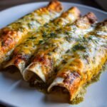 Three baked Green Chicken Enchiladas covered in melted cheese and green salsa, garnished with herbs.