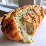 Close-up of Cheesy Herbed Garlic Bread with melted cheese stretching out from the scored loaf.