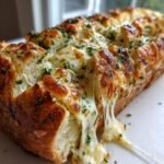 Close-up of Cheesy Herbed Garlic Bread with melted cheese stretching out from the cuts.