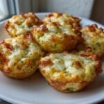 Close-up of several golden brown Cheesy Zucchini Tomato Bites topped with melted, bubbly cheese.