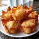 A close-up of several crispy, golden-brown Crab Rangoon Bombs piled on a white plate.