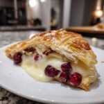 A close-up of a slice of Cranberry Pecan Brie In Flaky Puff Pastry with melted cheese oozing out.