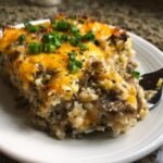 A close-up of a serving of Creamy Beef Mushroom Rice Bake topped with melted cheddar cheese and chopped green onions.