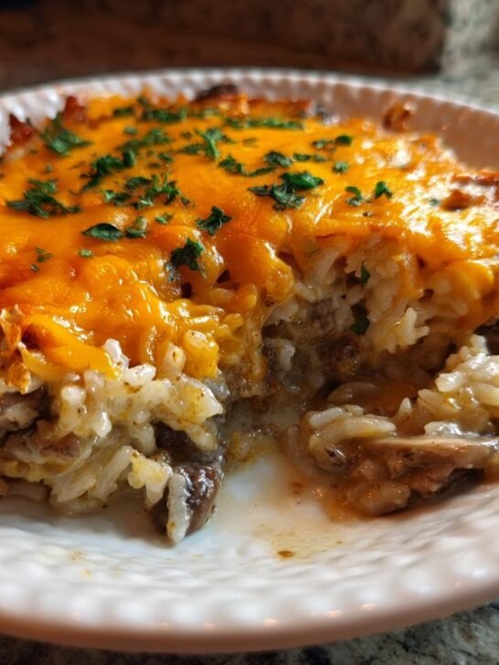 A serving of Creamy Beef Mushroom Rice Bake topped with melted cheddar cheese and parsley on a white plate.