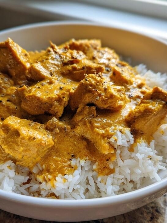 A white bowl filled with fluffy white rice topped generously with rich, orange Creamy Butternut Squash Butter Chicken.