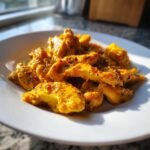 Close-up of tender chicken pieces coated in a rich, yellow Creamy Butternut Squash Butter Chicken sauce, sprinkled with pepper.