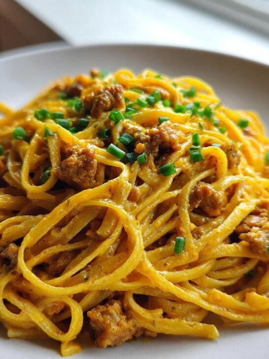 A close-up of Creamy Cowboy Butter Chicken Linguine tossed in a rich, orange sauce and topped with chopped chives.