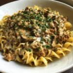 A close-up of a bowl filled with Creamy Turkey Stroganoff served over wide egg noodles and topped with fresh parsley.